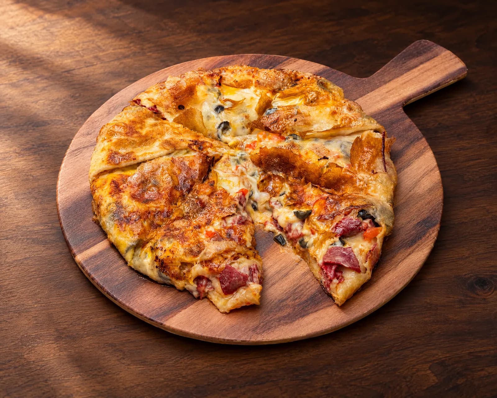 Basterma feteer cut into wedges on a wooden serving board